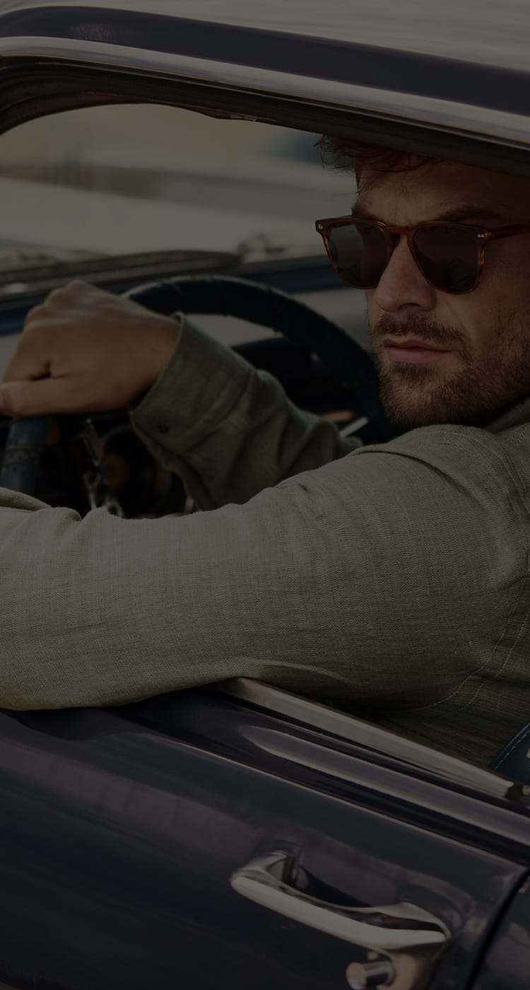 Man with sunglasses driving a blue car, wearing a green shirt, looking out the window.