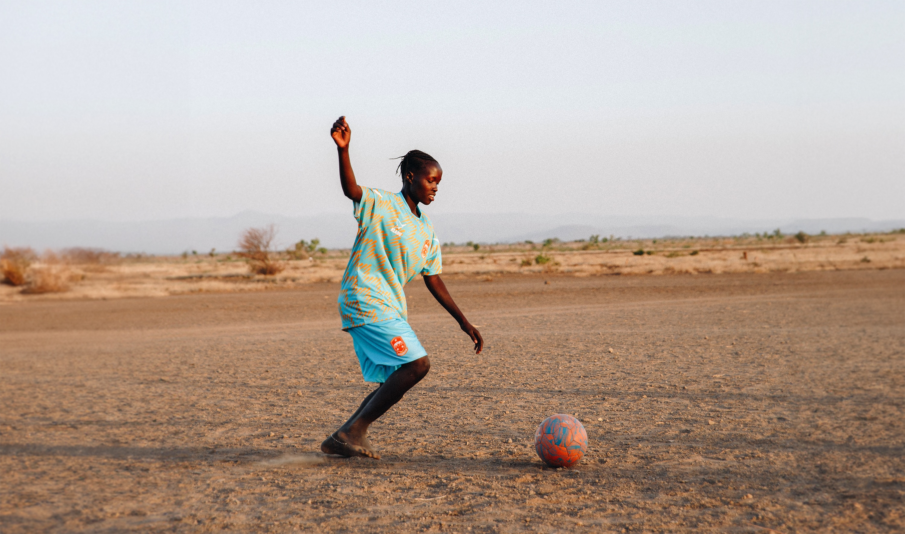 Girl kicking a football and wearing vibrant sportswear in Kenya